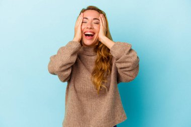 Mavi arka planda izole edilmiş beyaz kadın ellerini başının üstünde tutarak neşe içinde gülüyor. Mutluluk kavramı.