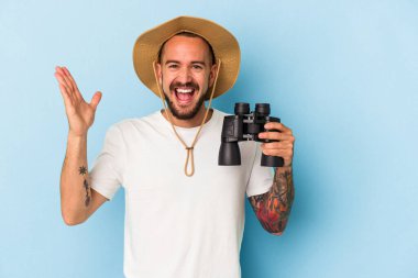 Mavi arka planda dürbün tutan beyaz dövmeli genç bir adam hoş bir sürprizle karşılaşıyor, heyecanlı ve el kaldırıyor..