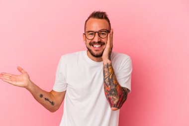 Pembe arka planda dövmeleri olan beyaz bir genç avucunun içinde fotokopi alanı tutuyor, el üstünde tutuyor. Şaşırmış ve mutlu..