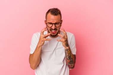 Pembe arka planda izole edilmiş dövmeleri olan genç beyaz adam gergin elleriyle çığlık atıyor..