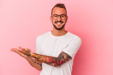 Pembe arka planda izole edilmiş dövmeleri olan genç beyaz bir adam palmiye ağacında bir kopya alanı tutuyor..