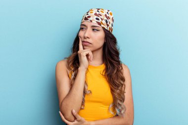 Genç Meksikalı kadın mavi arka planda izole edilmiş. Bir strateji planlıyor, bir iş yolu düşünüyor..