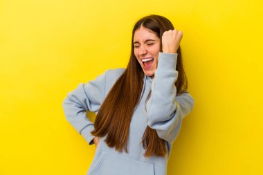 Sarı arka planda izole edilmiş genç beyaz kadın zaferi, tutkuyu ve coşkuyu kutluyor, mutlu bir ifade..