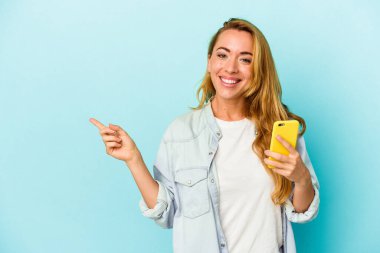 Mavi arka planda cep telefonu tutan beyaz kadın gülümsüyor ve boş alanda bir şey gösteriyor..