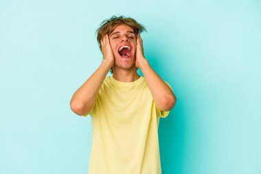 Mavi arka planda soyutlanmış beyaz makyajlı genç bir adam mutlu bir şekilde ellerini başının üstünde tutarak gülüyor. Mutluluk kavramı.