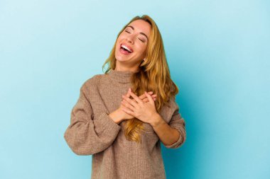 Mavi arka planda izole edilmiş beyaz kadın avuçlarını göğsüne bastıran dostça bir ifadeye sahip. Aşk konsepti.