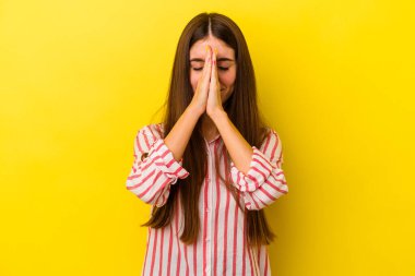 Sarı arka planda izole edilmiş genç, beyaz bir kadın el ele tutuşup ağzının kenarında dua ediyor, kendinden emin..