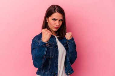 Pembe arka planda izole edilmiş genç beyaz kadın yumruğunu kameraya gösteriyor, agresif yüz ifadesi..