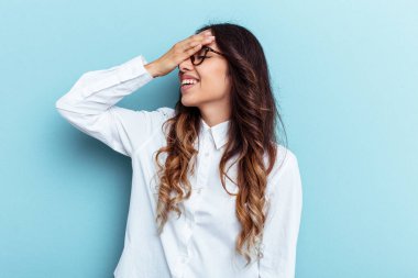 Mavi arka planda izole edilmiş genç Meksikalı kadın mutlu bir şekilde ellerini başının üstünde tutuyor. Mutluluk kavramı.