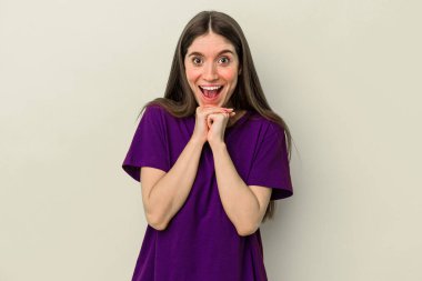 Beyaz tenli genç bir kadın sarı arka planda izole edilmiş şans diliyor, şaşırmış ve ağzını açıp önüne bakıyor..