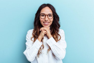 Genç Meksikalı kadın mavi arka planda izole edilmiş şans için dua ediyor, şaşırmış ve ağzını açıyor..