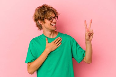 Makyajlı beyaz bir adam pembe arka planda izole edilmiş yemin ediyor, elini göğsüne koyuyor..