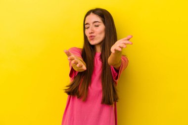 Sarı arka planda izole edilmiş genç, beyaz bir kadın. Dudaklarını kıvırıyor, avuç içlerini tutuyor ve hava öpücüğü yolluyor..