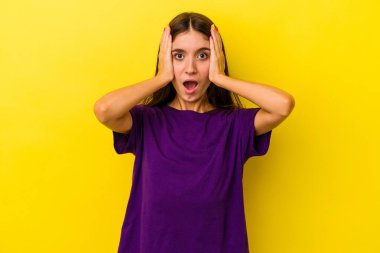 Sarı arka planda izole edilmiş genç, beyaz bir kadın. Kulakları kulaklarıyla kapatıyor. Çok fazla ses duymamaya çalışıyor..