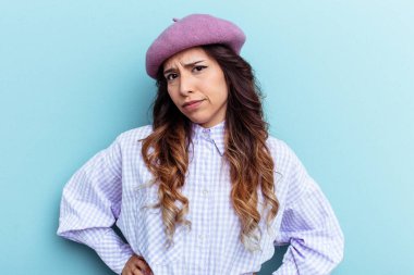 Mavi arka planda izole edilmiş genç Meksikalı kadın kafası karışmış, şüpheli ve güvensiz hissediyor..