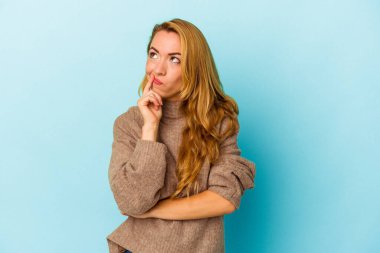 Mavi arka planda izole edilmiş beyaz bir kadın şüpheli ve şüpheci bir ifadeyle yana bakıyor..