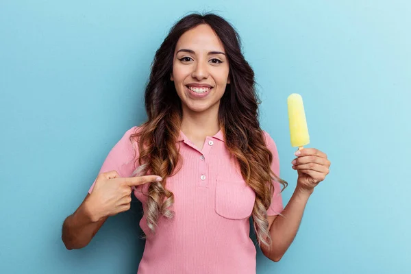 青い背景の人に手で指差すシャツのコピースペースにアイスクリームを保持若いラテン女性 誇りと自信 — ストック写真