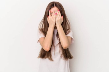 Beyaz arka planda izole edilmiş genç beyaz kadın kameraya parmaklarıyla göz kırpıyor, yüzünü kapatmaktan utanıyor..