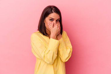 Pembe arka planda izole edilmiş genç, beyaz bir kadın elleri endişeli bir şekilde ağzı örtüyor..