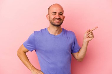 Kafkasyalı kel adam pembe arka planda izole edilmiş. Gülümsüyor ve işaret parmağıyla işaret ediyor..