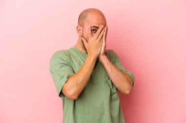 Genç beyaz kel adam pembe arka planda izole edilmiş. Korkmuş ve gergin parmaklarıyla göz kırp..