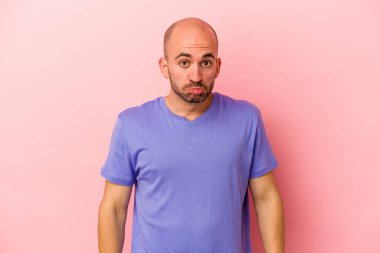 Pembe arka planda soyutlanmış beyaz kel bir adam omuzlarını silkeliyor ve gözleri açık..