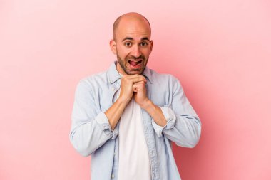 Kafkasyalı genç kel adam pembe arka planda izole edilmiş şans diliyor, şaşırıyor ve ağzını açıyor..