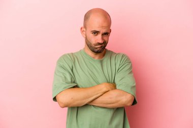 Kafkasyalı genç kel adam pembe arka planda izole edilmiş hoşnutsuzca kaşlarını çatmış, kollarını kavuşturmuş..