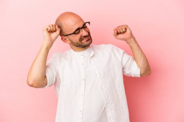 Kafkasyalı genç kel adam pembe arka planda izole edilmiş özel bir günü kutluyor, atlıyor ve enerjiyle kollarını kaldırıyor..