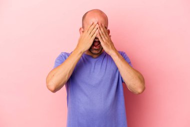 Pembe arka planda soyutlanmış beyaz tenli genç bir adam elleriyle gözlerini kapatıyor, gülümseyerek bir sürpriz bekliyor..