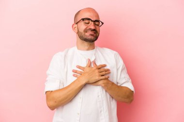 Pembe arka planda soyutlanmış beyaz kel bir adam gülüyor, elini yüreğine koyuyor, mutluluk kavramını koruyor..