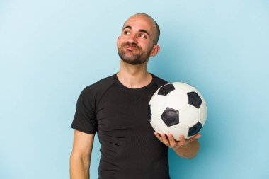 Genç iş adamı kel adam mavi arka planda izole bir şekilde futbol oynuyor. Hedeflerine ve amaçlarına ulaşmayı hayal ediyor.