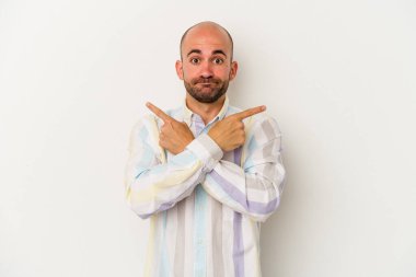 Beyaz arka planda izole genç kel adam, iki seçenek arasında seçim yapmaya çalışıyor.