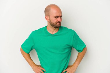 Beyaz arka planda soyutlanmış genç kel bir adam kafası karışmış, şüpheli ve güvensiz hissediyor..