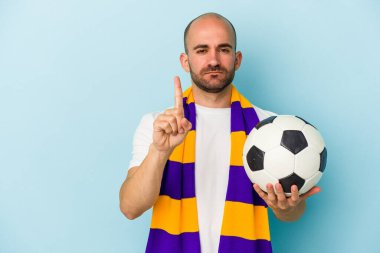 Mavi arka planda izole edilmiş atkı takan genç ve kel bir adam bir numarayı parmağıyla gösteriyor..