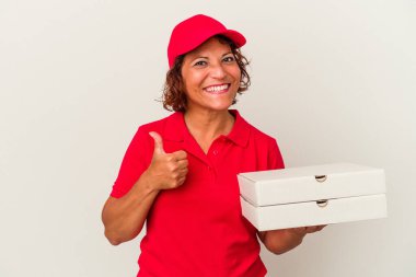 Orta yaşlı teslimatçı kadın beyaz arka planda izole pizzalar alıyor gülümsüyor ve başparmağını kaldırıyor.