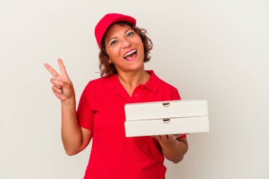 Beyaz arka planda izole pizzalar yiyen orta yaşlı kadın neşeli ve kaygısız parmaklarıyla barış sembolü gösteriyor..