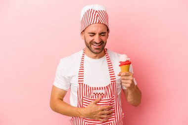 Dondurma yapan genç adam pembe arka planda izole edilmiş dondurma tutuyor. Gülüyor ve eğleniyor..