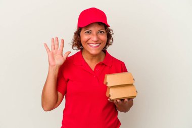 Beyaz arka planda izole edilmiş burgerleri alan orta yaşlı teslimatçı kadın gülümseyerek beş numarayı parmaklarıyla gösteriyor..