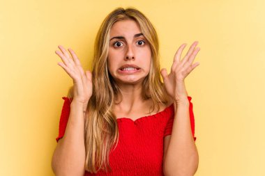 Sarışın, sarı arka planda izole edilmiş genç bir kadın gökyüzüne haykırıyor, yukarı bakıyor, hayal kırıklığına uğruyor..