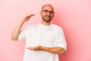 Kafkasyalı genç kel adam pembe arka planda izole edilmiş. Elinde parmakları olan, gülümseyen ve kendinden emin bir şey var..