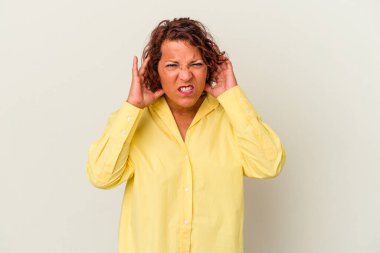 Beyaz arka planda izole edilmiş orta yaşlı Latin bir kadın parmaklarıyla kulaklarını kapatıyor, gürültülü bir ortam yüzünden stresli ve çaresiz..