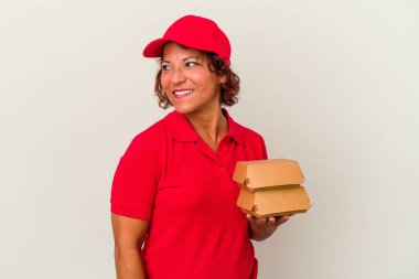 Beyaz arka planda soyulmuş burgerleri alan orta yaşlı bir kadın gülümsüyor, neşeli ve keyifli görünüyor..