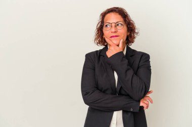 Beyaz arka planda izole edilmiş orta yaşlı Latin iş kadını şüpheli ve şüpheci bir ifadeyle yana bakıyor..