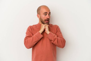 Genç kel adam beyaz arka planda izole edilmiş şans için dua ediyor, şaşkın ve ağzı açık bir şekilde önüne bakıyor..