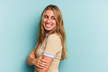 Genç, beyaz, sarışın bir kadın mavi arka planda izole edilmiş, gülüyor ve eğleniyor..