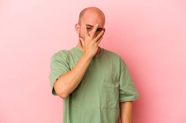 Kafkasyalı genç kel adam pembe arka planda izole edilmiş parmaklarıyla kameraya göz kırpıyor, yüzünü kapatmaktan utanıyor..