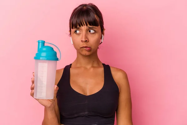 ピンクの背景に隔離されたタンパク質を飲む若い混合人種の女性は混乱し 疑問と不確定な感じ — ストック写真