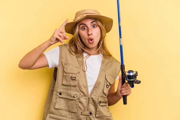 年轻的高加索金发女渔民手持一根被黄色背景隔离的棒子 有一个想法 灵感的概念 — 图库照片