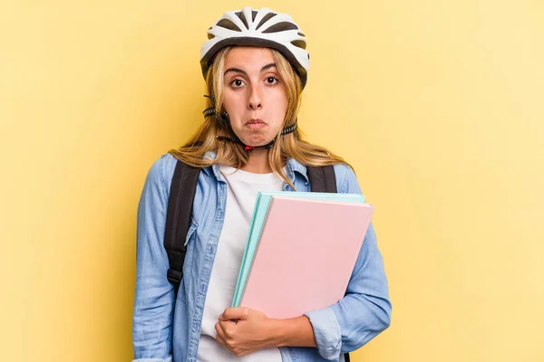 若いですCaucasian学生女性身に着けていますAバイクヘルメット絶縁上の黄色の背景Shrugs肩とオープン目混乱 — ストック写真